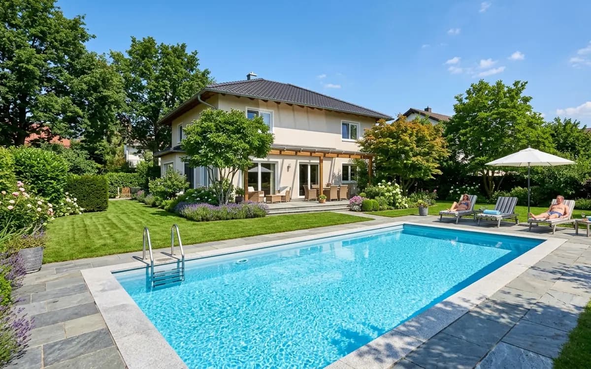 Rechteckiger Gartenpool mit Natursteinumrandung hinter einem Einfamilienhaus